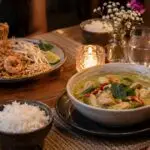 Intimate anniversary dinner table for two, Thai green curry and Pad Thai, two water glasses, subtle small flowers