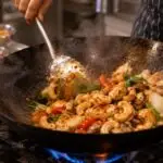 Thai cook stir-frying one small portion of chicken with cashews onions mushrooms and sweet chilli in a hot wok